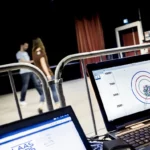 Photo de personnes se déplaçant dans une pièce et d'écrans de controle